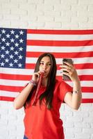 mulher com um fazedor de barulho tirando uma selfie no fundo da bandeira dos EUA foto