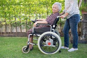médico ajuda paciente idosa asiática sentada em cadeira de rodas no parque foto
