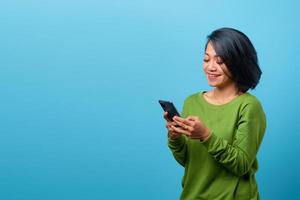 linda mulher asiática sorrindo usando telefone celular em fundo azul foto