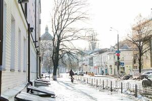 Kyiv, Ucrânia-25.12.17 rua depois de queda de neve. não limpo a partir de a neve faixas. gelo em a calçada. Visão do a Igreja dentro inverno geadas dentro Kiev em podol. ciclista em a planador coberto de gelo estrada. foto