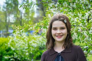 lindo menina entre cereja flores dentro Primavera. retrato do uma menina com Castanho cabelo e verde olhos. foto