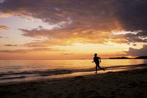 silhueta do feliz homem corrida em a de praia às pôr do sol foto