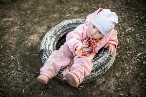 bebê dentro borracha pneu a partir de roda. pequeno menina alcança fora. criança pergunta para ajuda. 1 ano velho menina jogando ao ar livre Parque infantil danificar para pneus para saúde. foto