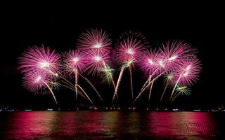 incríveis e lindos fogos de artifício coloridos na noite de celebração, mostrando na praia do mar com reflexo de várias cores na água foto