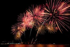 incríveis e lindos fogos de artifício coloridos na noite de celebração, mostrando na praia do mar com reflexo de várias cores na água foto