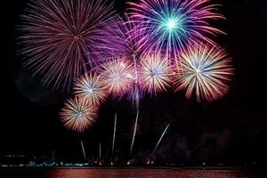 incríveis e lindos fogos de artifício coloridos na noite de celebração, mostrando na praia do mar com reflexo de várias cores na água foto