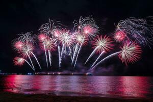 incríveis e lindos fogos de artifício coloridos na noite de celebração, mostrando na praia do mar com reflexo de várias cores na água foto