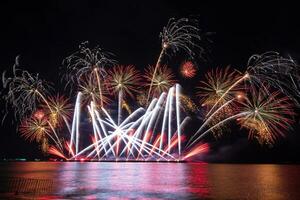 incríveis e lindos fogos de artifício coloridos na noite de celebração, mostrando na praia do mar com reflexo de várias cores na água foto