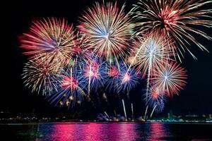 incríveis e lindos fogos de artifício coloridos na noite de celebração, mostrando na praia do mar com reflexo de várias cores na água foto