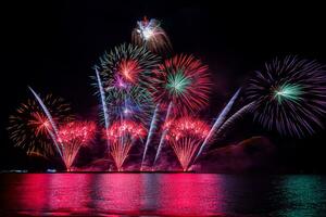 incríveis e lindos fogos de artifício coloridos na noite de celebração, mostrando na praia do mar com reflexo de várias cores na água foto