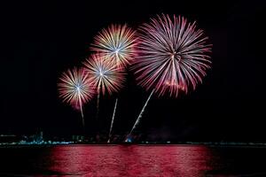 incríveis e lindos fogos de artifício coloridos na noite de celebração, mostrando na praia do mar com reflexo de várias cores na água foto