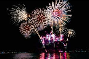 incríveis e lindos fogos de artifício coloridos na noite de celebração, mostrando na praia do mar com reflexo de várias cores na água foto