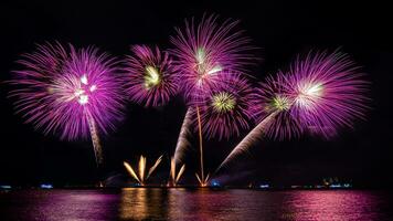 incríveis e lindos fogos de artifício coloridos na noite de celebração, mostrando na praia do mar com reflexo de várias cores na água foto