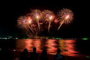 incríveis e lindos fogos de artifício coloridos na noite de celebração, mostrando na praia do mar com reflexo de várias cores na água foto