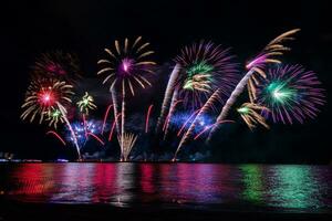 incríveis e lindos fogos de artifício coloridos na noite de celebração, mostrando na praia do mar com reflexo de várias cores na água foto