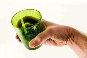 uma mão segurando acima uma verde vidro com uma verde líquido dentro foto