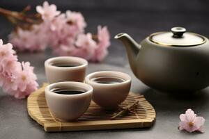 tradicional cerimônia. copos do fabricado chá, chaleira e sakura flores em cinzento mesa. generativo ai foto