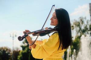 mulher artista com Sombrio cabelo dentro uma vestir tocam uma de madeira show elétrico violino foto