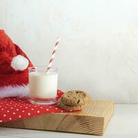 vidro leite, biscoitos, vermelho santa chapéu, vermelho polca ponto guardanapo em de madeira borda. leite para papai noel. cópia de espaço foto