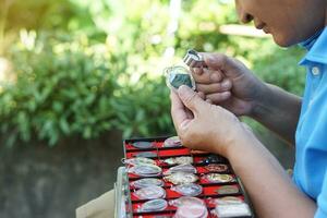 ásia homem é inspecionando Buda amuletos a partir de dele coleções de usando mini ampliação vidro. conceito, fé e crença dentro piedosos e sorte para budistas. coleta amuleto Como hobbies, troca ou troca. foto