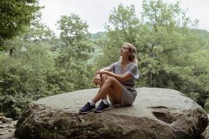 mulher sentada em uma grande pedra na floresta, descansando ou meditando foto