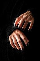 Mulher assustadora com mãos de halloween com unhas pretas em fundo escuro foto