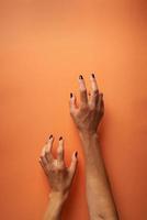 Mulher assustadora com mãos de halloween com unhas pretas em fundo laranja foto