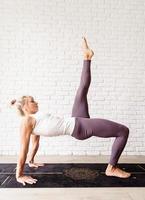 mulher loira praticando ioga em casa, fazendo ponte para os glúteos