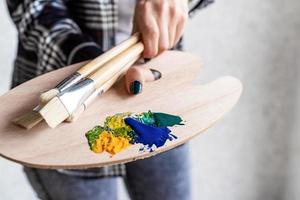 close-up das mãos do artista segurando uma paleta de arte em madeira e pincéis foto