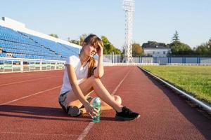 adolescente sentada na pista do estádio, descansando água potável foto