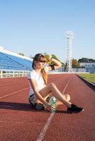 adolescente sentada na pista do estádio, descansando água potável foto