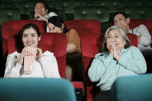 vários pessoas dentro teatro. ásia Senior mulher e muitos audiências estão assustado do assistindo suspense e Horror cinema, assustado juntos em filme estágio, e entretenimento estilo de vida com filme mostrar. foto