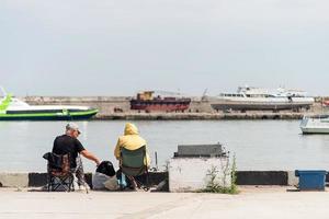 pessoas pescando no aterro, barcos e iates ao fundo foto