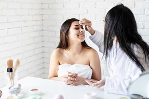 duas lindas mulheres aplicando creme facial fazendo procedimentos de spa foto