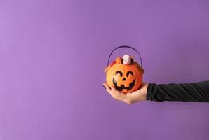 mão de mulher de halloween com unhas pretas segurando uma abóbora cheia de doces foto