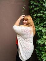 mulher com sobrepeso posando em uma parede sólida marrom na rua foto