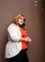 mulher com sobrepeso posando em uma parede sólida marrom na rua foto