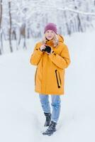 feliz menina fotógrafo dentro uma amarelo Jaqueta leva As fotos do inverno dentro uma Nevado parque