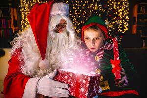 santa claus abertura uma pacote cheio do Natal Magia poeira juntos com uma jovem duende foto