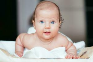 retrato do uma lindo bebê menina mentiras em uma branco Folha dentro dela quarto foto