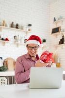 homem com chapéu de Papai Noel cumprimentando seus amigos no chat por vídeo ou ligar no laptop foto