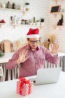 homem com chapéu de Papai Noel cumprimentando seus amigos no chat por vídeo ou ligar no laptop foto