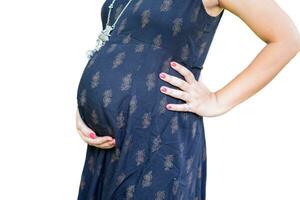 uma grávida indiano senhora poses para gravidez tiro e mãos em barriga com branco fundo, indiano grávida mulher coloca dela mão em dela estômago dentro maternidade vestir com avião fundo, gravidez tiro foto