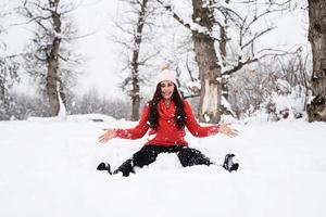 jovem morena de suéter vermelho brincando com a neve no parque foto