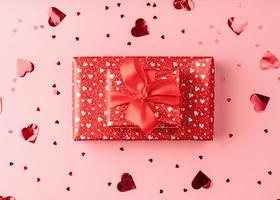 caixa de presente vermelha com laço de corda no fundo rosa com confete de coração