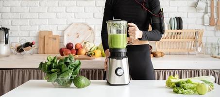 jovem loira sorridente fazendo suco verde na cozinha de casa foto