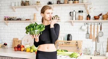 mulher com roupas esportivas segurando uma tigela de espinafre fresco na cozinha foto