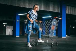 mulher vestida de jeans com carrinhos de compras no estacionamento