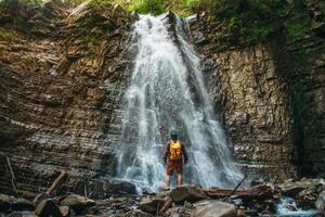 homem com uma mochila perto de uma cachoeira foto