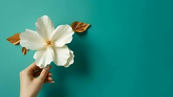 mão segurando uma branco flor com ouro folhas contra uma cerceta fundo foto